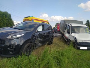 Na zdjęciu widać od lewej samochód osobowy kia z uszkodzeniami jakie powstały w wyniku uderzenia i wystrzeloną poduszką powietrzną. Za tym samochodem widać górę karetki pogotowia. Następnie po lewej stronie widać drugi samochód marki Iveco z widocznymi uszkodzeniami powstałymi na skutek zdarzenia drogowego. Samochody te są poza drogą.