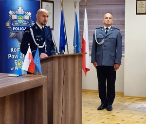 Na zdjęciu za mównicą widać prowadzącego uroczystość aspiranta Tomasza Hałkę. W tle po prawej stronie Dowódca uroczystości aspirant sztabowy Dariusz Maślanka.