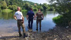 Na zdjęciu widoczni funkcjonariusze Straży Rybackiej oraz policjant stojący nad rzeką i kontrolujący rejon. Dookoła widoczna gospodarka drzewna nad akwenem.