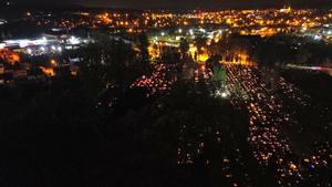 Zdjęcie wykonane z lotu ptaka w porze nocnej. Na zdjęciu widoczny jest teren cmentarza komunalnego w Brzozowie, na którym widać rozświetlone znicze ustawione na płytach nagrobnych. Po lewej stronie ciemne miejsce stanowią zadrzewienia. Dalej w kadrze w tle widać teren miasta Brzozowa, który oświetlony jest miejską siecią latarni.