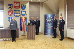 Zdjęcie przedstawia moment uroczystości podczas którego przemawia Komendant Wojewódzki Policji w Rzeszowie. Od lewej strony w pozycji zasadniczej stoi aspirant sztabowy Dariusz Maślanka pełniący funkcje dowódcy uroczystości, dalej za mównicą stoi Komendant Wojewódzki Policji w Rzeszowie inspektor Jarosław Tokarczyk, z tyłu w tle stoi aspirant Tomasz Hałka, który prowadził uroczystości jako lektor, następnie stoi zastępca Komendanta Powiatowego Policji w Brzozowie młodszy inspektor Marek Śliwiński i ostatni po prawej stronie stoi Komendant Powiatowy Policji w Brzozowie inspektor Mirosław Wośko