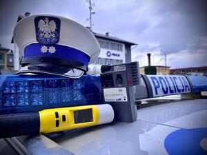 Na zdjęciu widać umieszczone na belce od radiowozu: czapkę policjanta ruchu drogowego, a przed nią ustawione na dachu radiowozu urządzenia do badania stanu trzeźwości typu: iBlow oraz Alkosensor, w tle rozmazany budynek Komendy Powiatowej Policji w Brzozowie