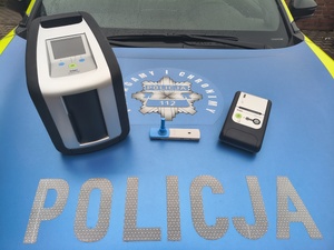 Na zdjęciu widoczne urządzenie Drug Test - pozwalające sprawdzić w próbce śliny substancji narkotycznych. Zdjęcie wykonane na pokrywie pojazdu służbowego, widoczny napis POLICJA.